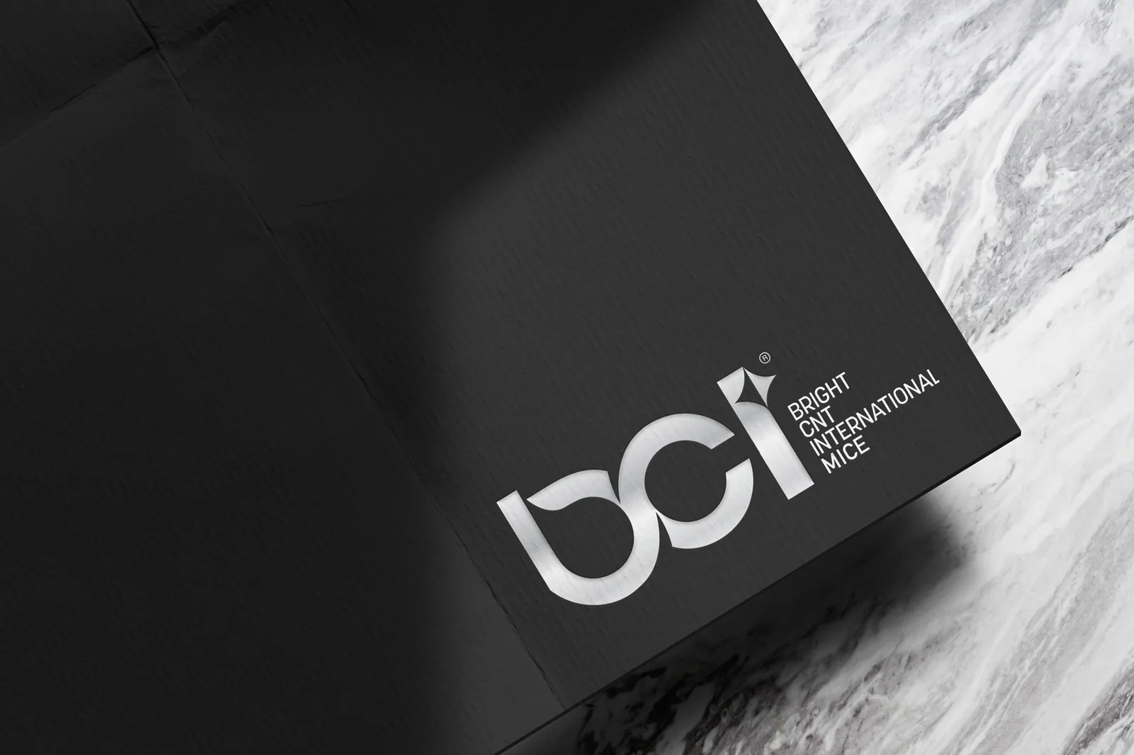 The BCI Bright CNT International MICE logo printed in silver on textured black paper, beside a marble surface