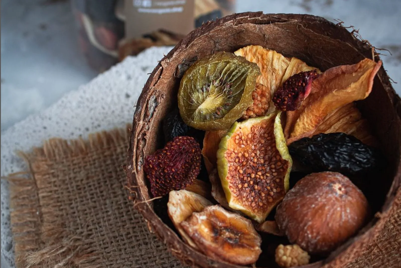 Dried figs, kiwi and fruit in a coconut-shell bowl on burlap